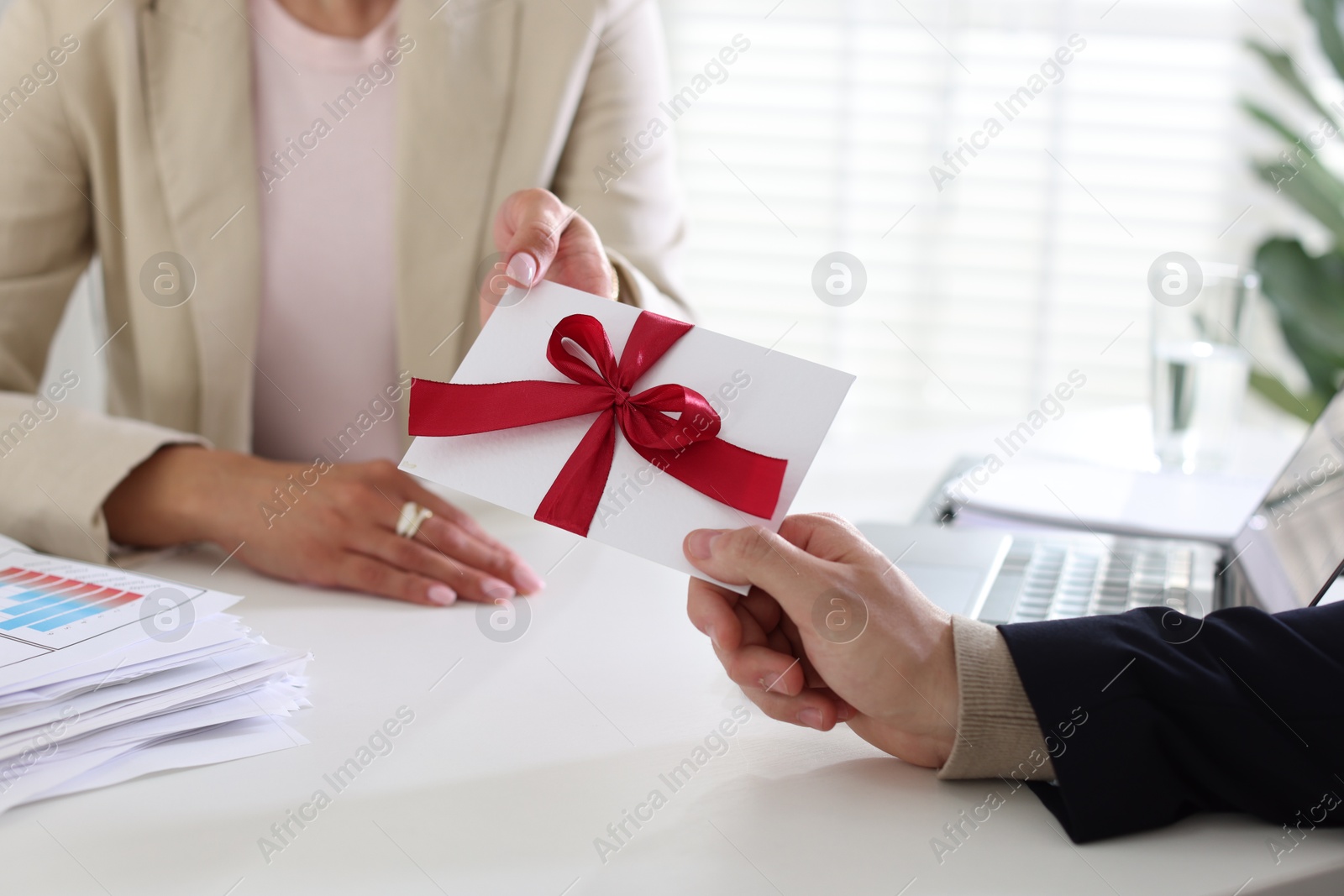 Money bonus. Boss giving envelope with bow to employee in office, closeup Photo of Money bonus. Boss giving envelope with bow to employee in office, closeup