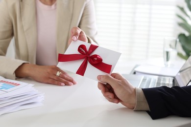 Photo of Money bonus. Boss giving envelope with bow to employee in office, closeup