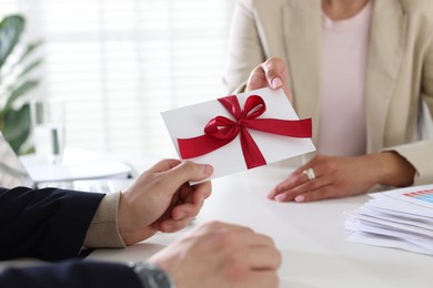 Photo of Money bonus. Boss giving envelope with bow to employee in office, closeup