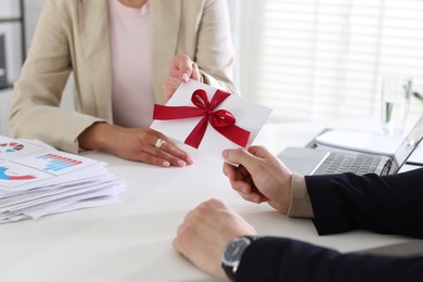 Photo of Money bonus. Boss giving envelope with bow to employee in office, closeup
