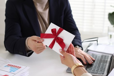 Photo of Money bonus. Employee receiving envelope with bow from boss in office, closeup