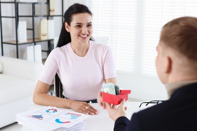 Photo of Bonus. Employee receiving box with money from boss in office