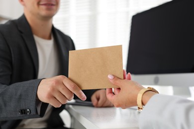 Photo of Money bonus. Boss giving envelope to employee in office, closeup