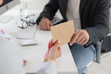 Photo of Money bonus. Boss giving envelope to employee in office, closeup