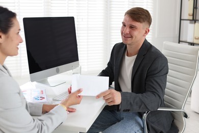 Photo of Money bonus. Employee receiving envelope from boss in office