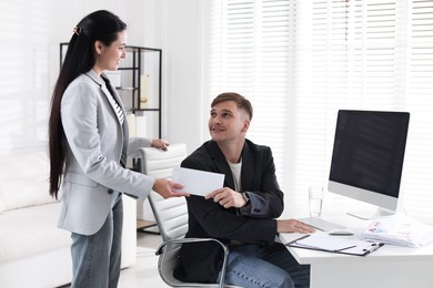 Photo of Money bonus. Employee receiving envelope from boss in office
