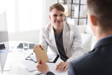 Photo of Money bonus. Employee receiving envelope from boss in office