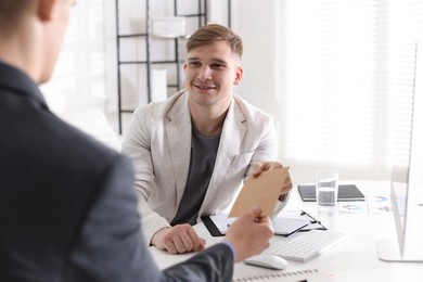 Photo of Money bonus. Employee receiving envelope from boss in office