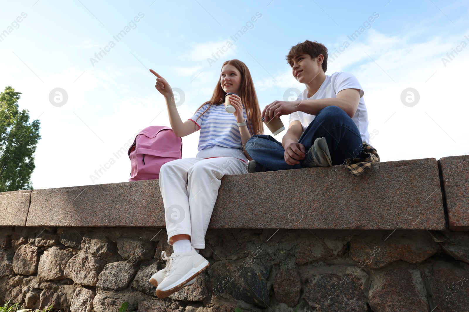 Teenage girl and boy with drinks outdoors, low angle view Photo of Teenage girl and boy with drinks outdoors, low angle view