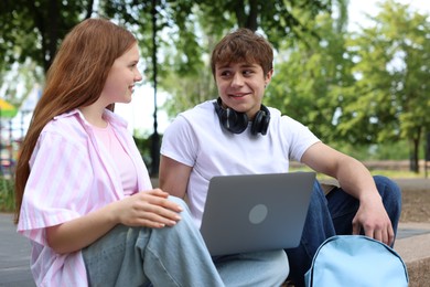 Photo of Teenage girl and boy with laptop outdoors