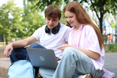 Photo of Teenage girl and boy with laptop outdoors