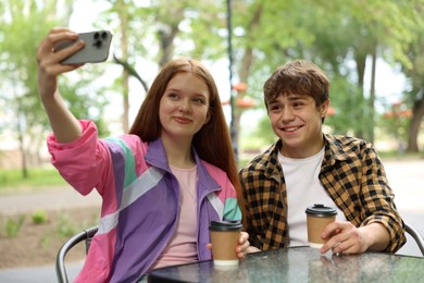 Photo of Teenage girl and boy taking selfie together in outdoor cafe