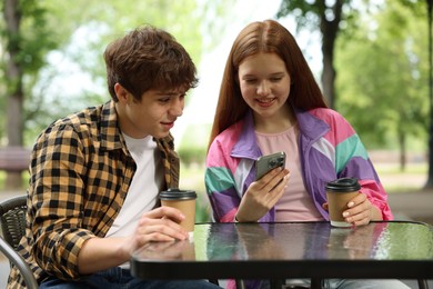 Photo of Teenage girl and boy with coffee and smartphone in outdoor cafe