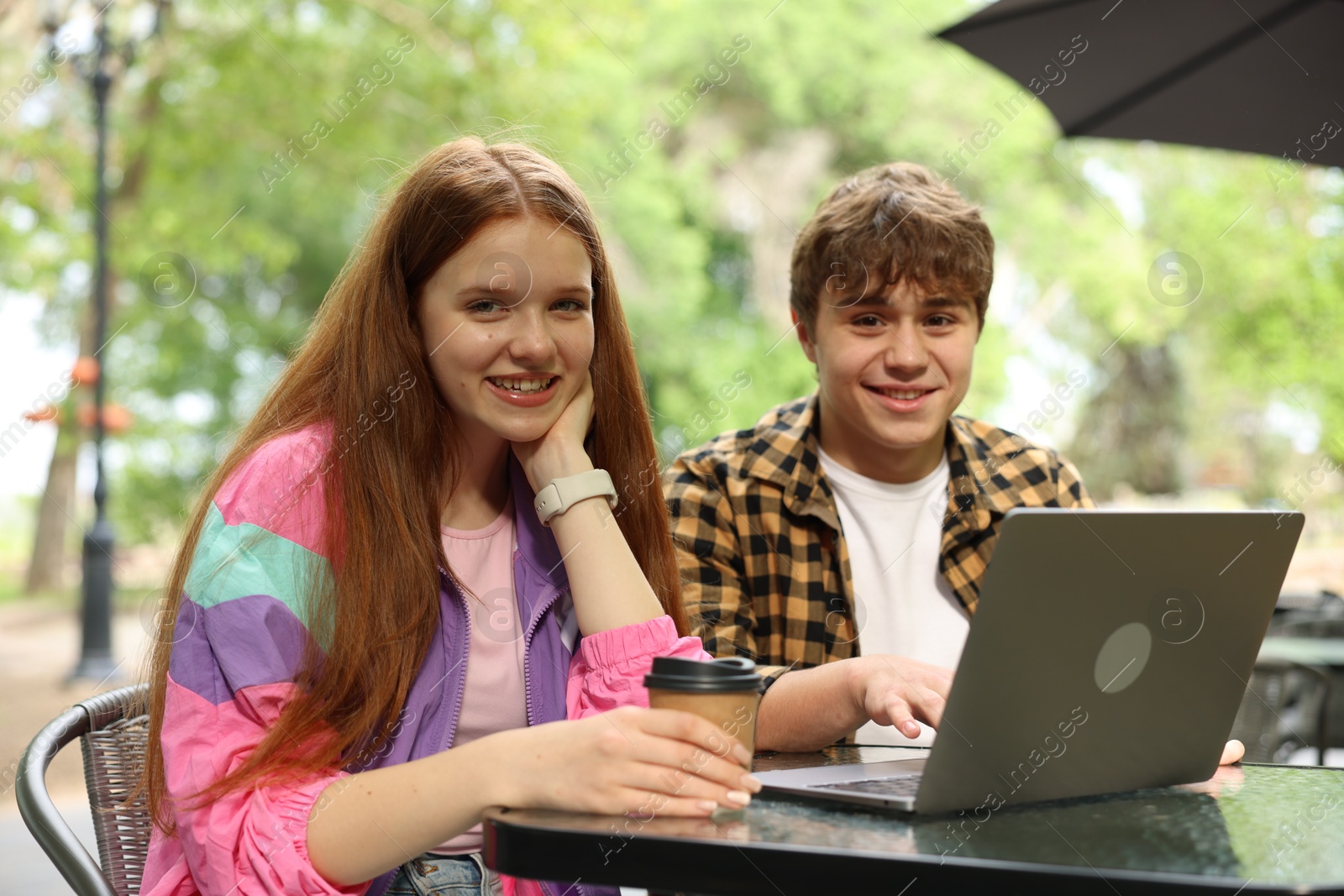Teenage girl and boy with coffee and laptop in outdoor cafe Photo of Teenage girl and boy with coffee and laptop in outdoor cafe