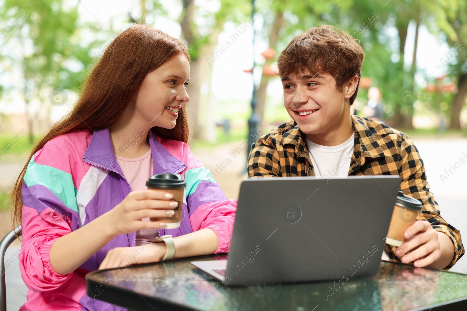 Teenage girl and boy with coffee and laptop in outdoor cafe Photo of Teenage girl and boy with coffee and laptop in outdoor cafe