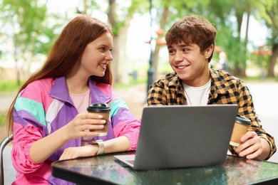 Photo of Teenage girl and boy with coffee and laptop in outdoor cafe