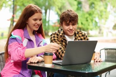 Photo of Teenage girl and boy with coffee and laptop in outdoor cafe
