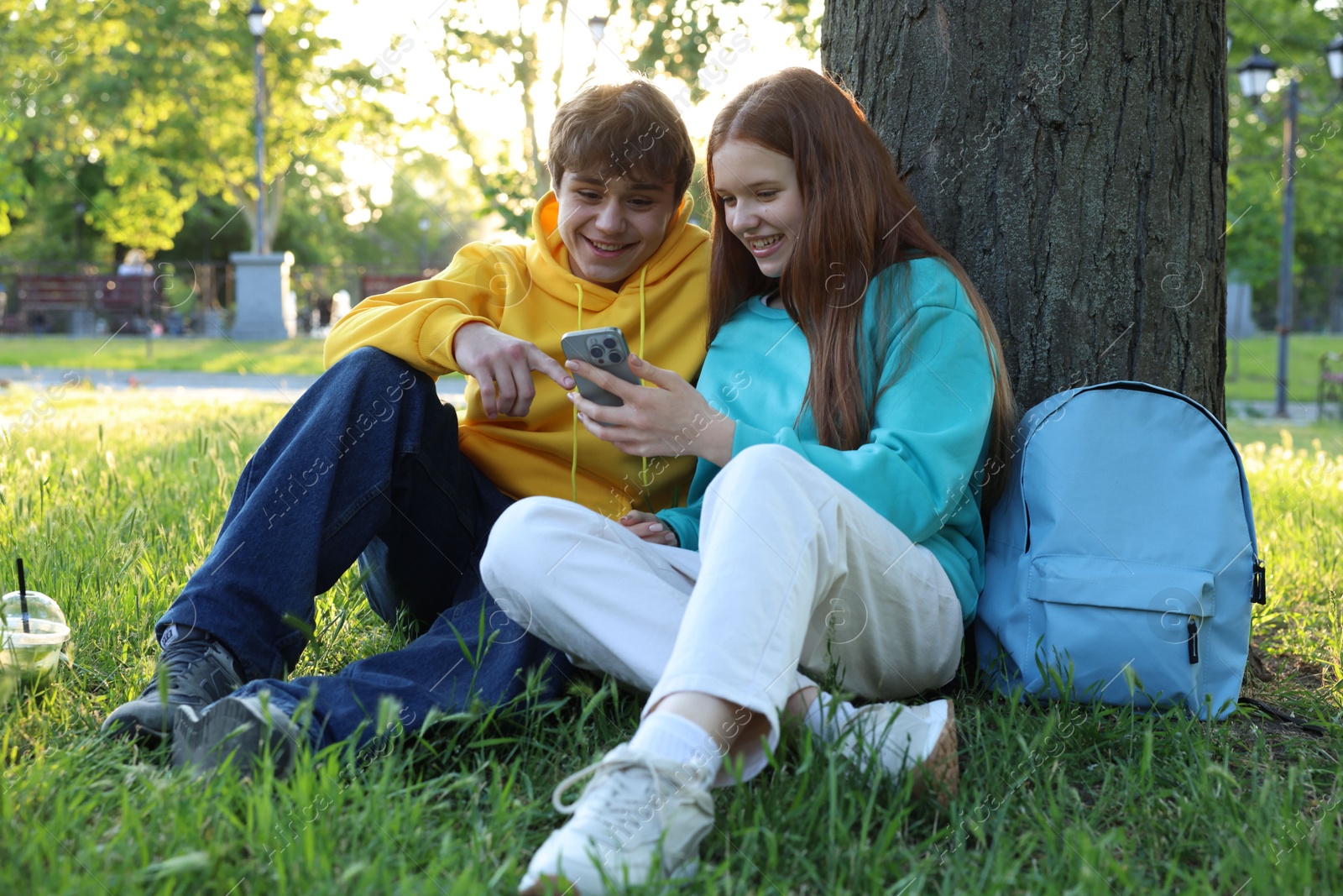 Photo of Teenage girl and boy with smartphone on green grass in park