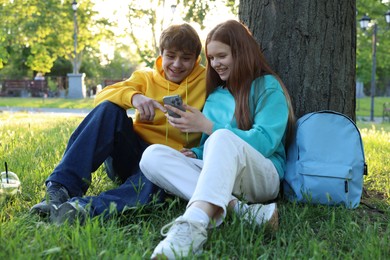 Photo of Teenage girl and boy with smartphone on green grass in park