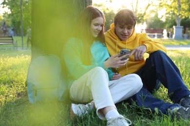 Photo of Teenage girl and boy with smartphone on green grass in park