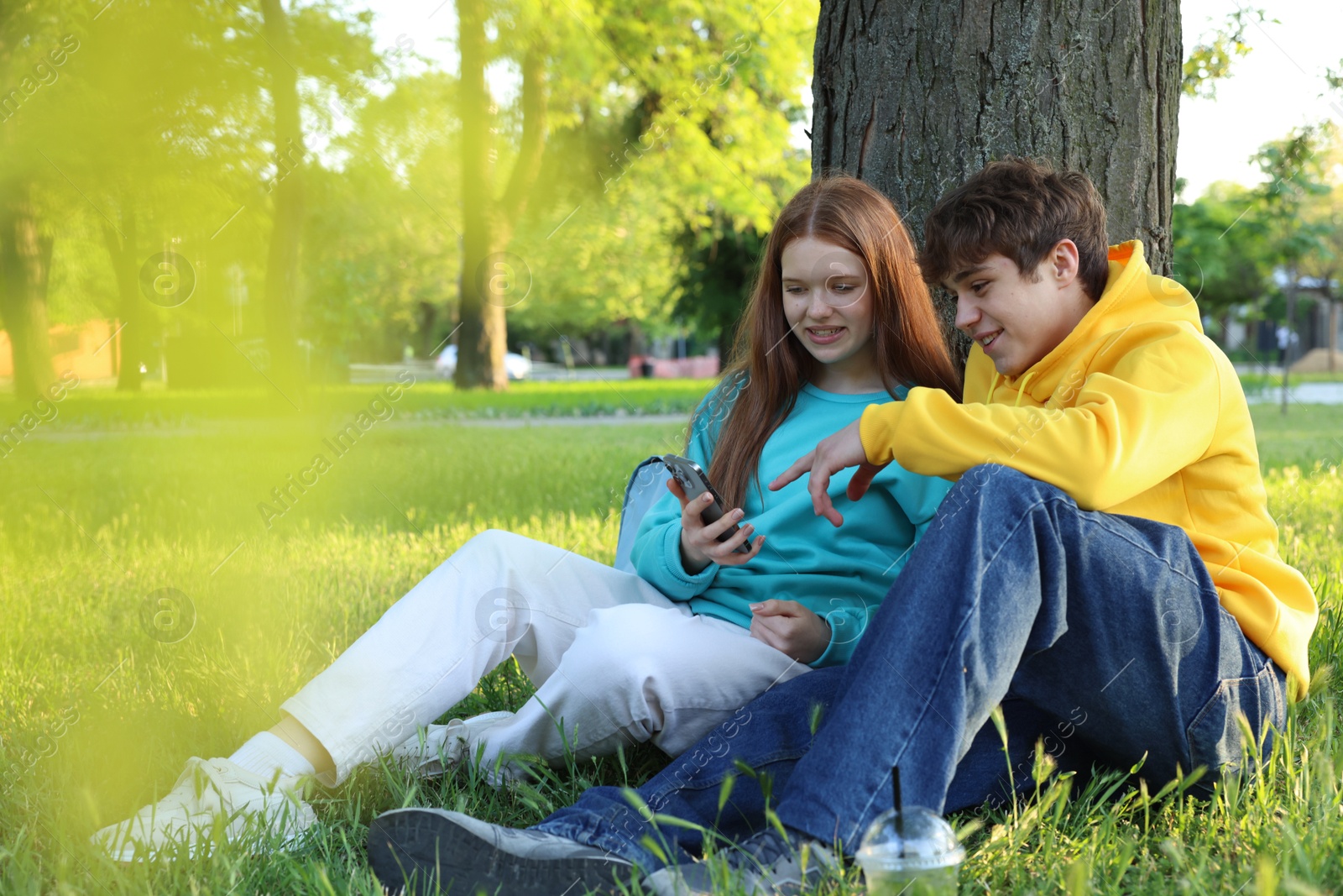 Teenage girl and boy with smartphone on green grass in park Photo of Teenage girl and boy with smartphone on green grass in park