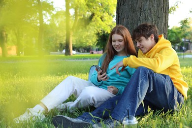 Photo of Teenage girl and boy with smartphone on green grass in park
