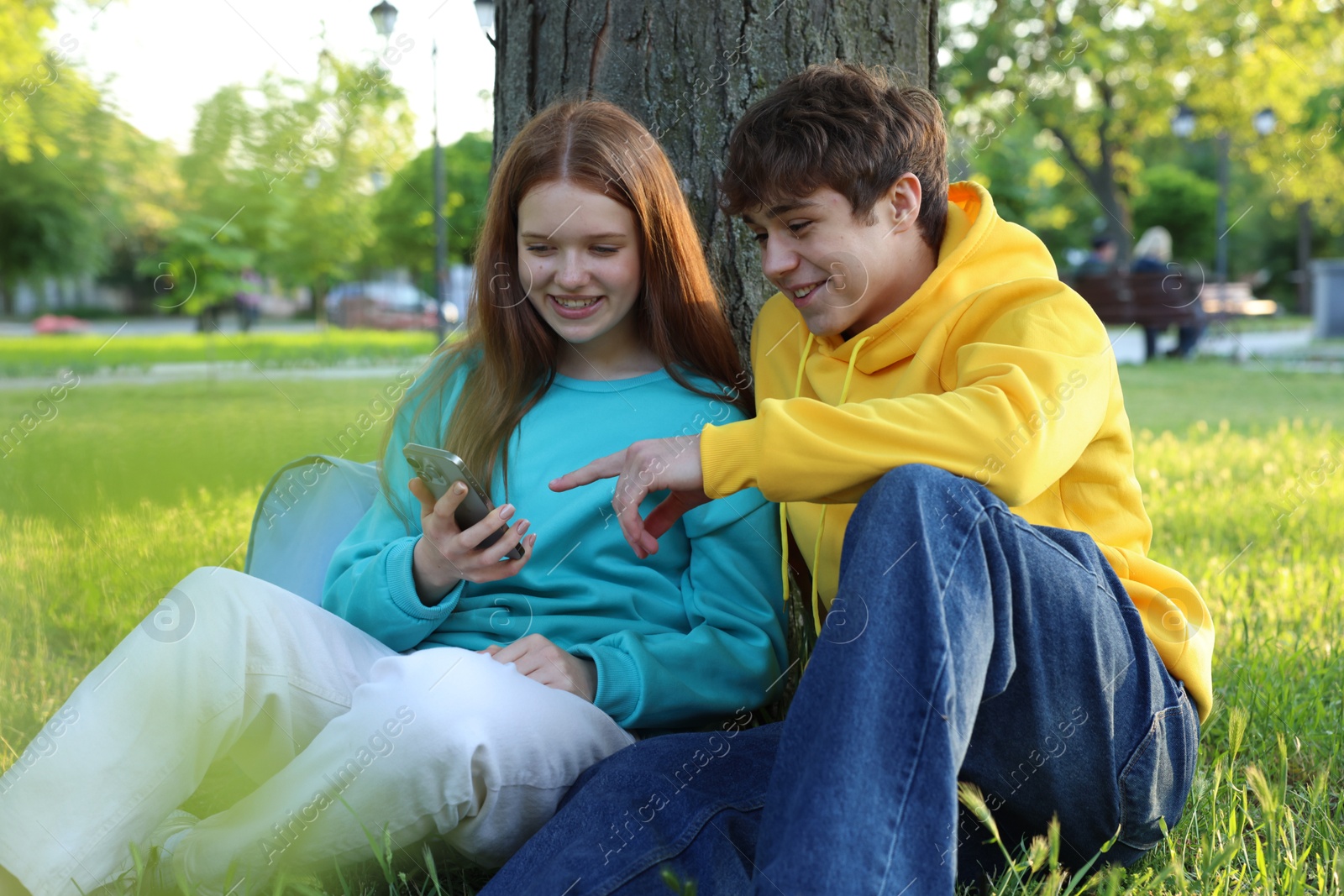 Teenage girl and boy with smartphone on green grass in park Photo of Teenage girl and boy with smartphone on green grass in park
