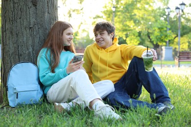 Photo of Teenage girl and boy with smartphone and drink on green grass in park