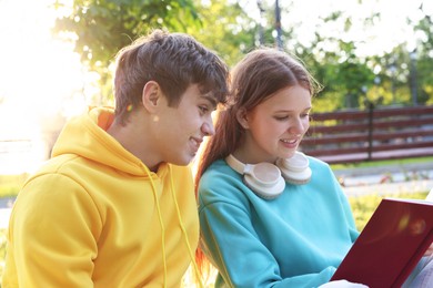 Photo of Teenage girl and boy reading together in park