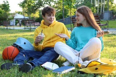 Photo of Teenage girl and boy with phone and books in park