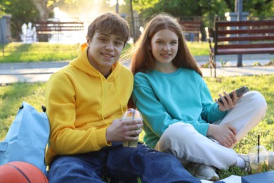 Photo of Teenage girl and boy with drinks and smartphone in park
