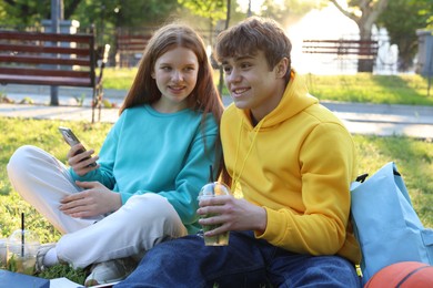 Photo of Teenage girl and boy with drinks and smartphone in park
