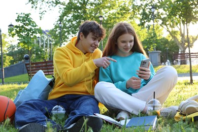 Photo of Teenage girl and boy with phone and books in park