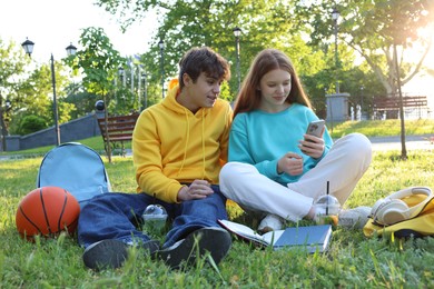 Photo of Teenage girl and boy with phone and books in park