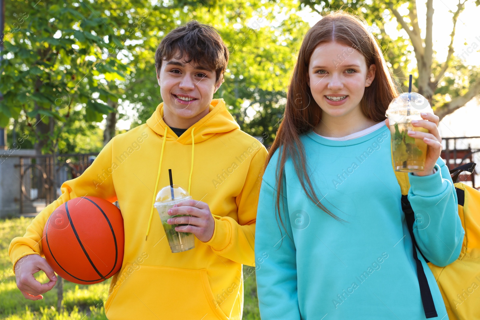 Teenage girl and boy with drinks and basketball in park Photo of Teenage girl and boy with drinks and basketball in park