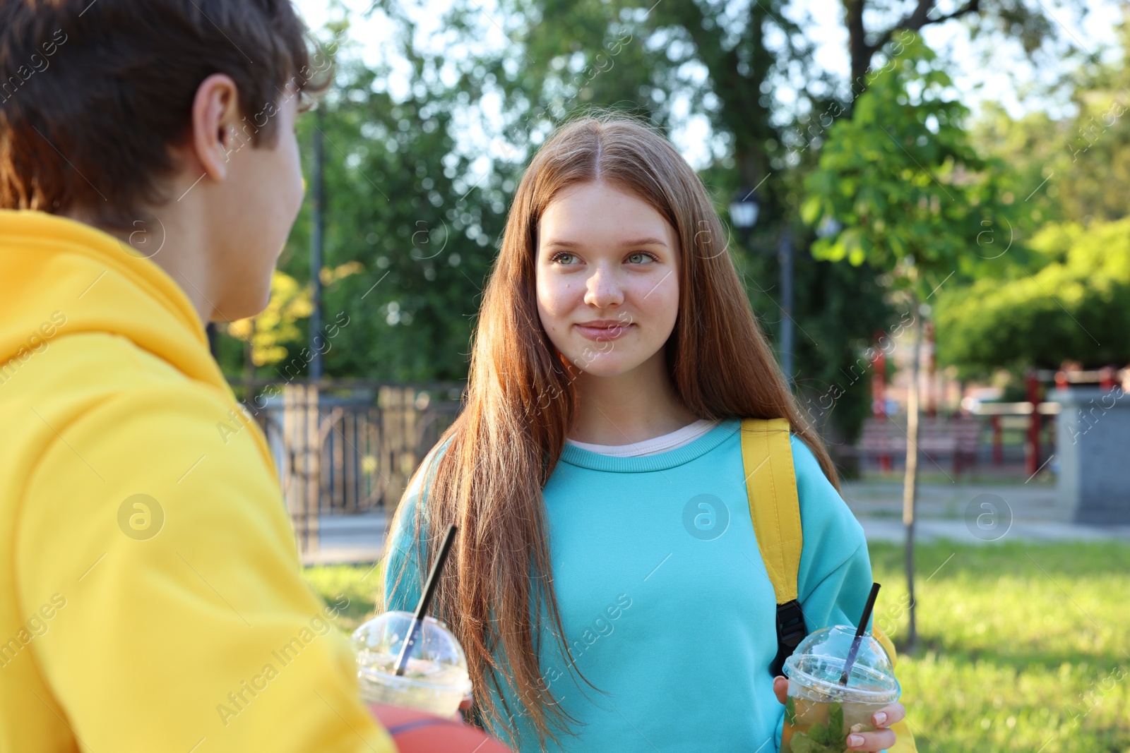 Teenage girl and boy with drinks in park Photo of Teenage girl and boy with drinks in park