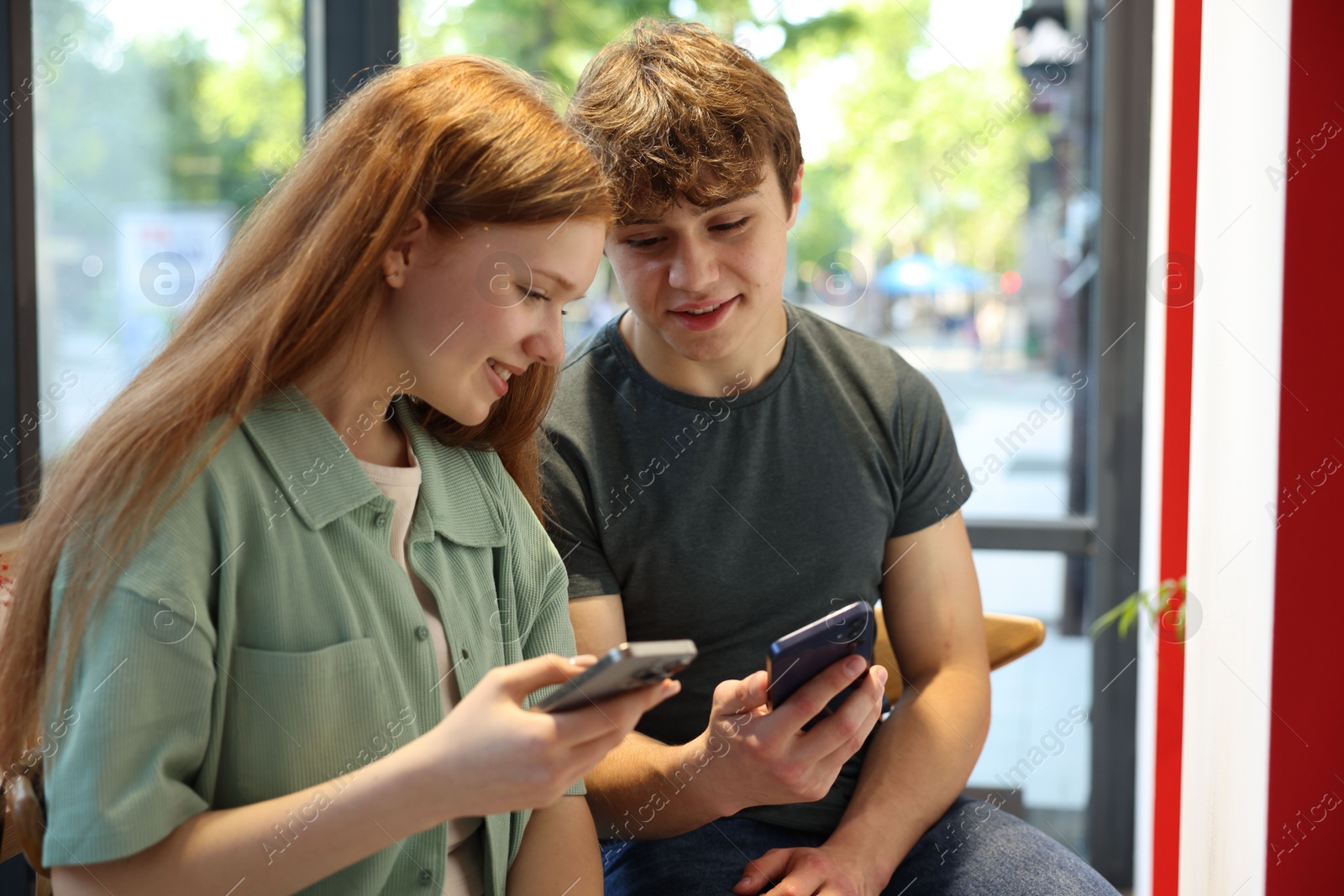 Teenage girl and boy with phones indoors Photo of Teenage girl and boy with phones indoors