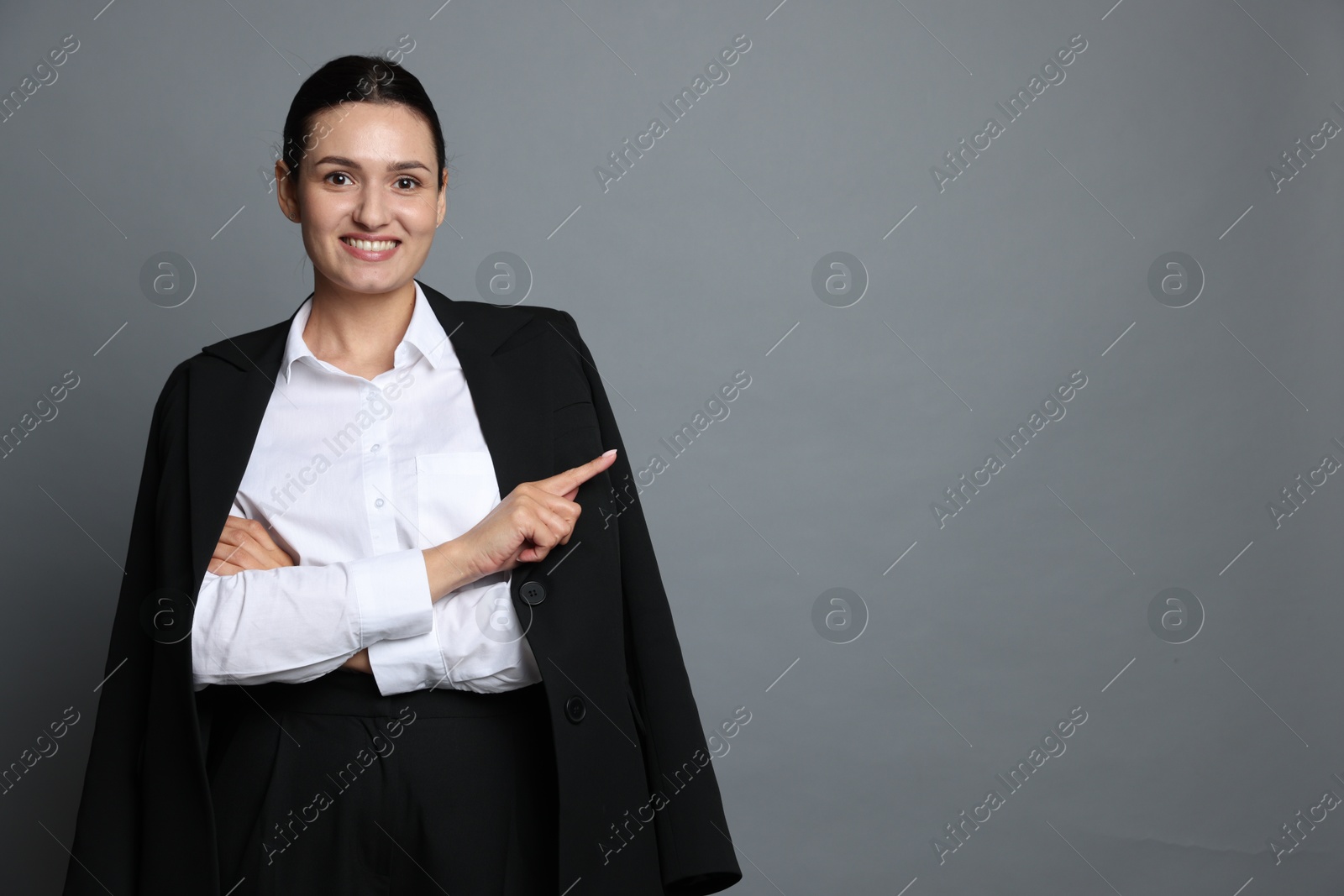 Confident business woman in suit pointing at something on grey background. Space for text Photo of Confident business woman in suit pointing at something on grey background. Space for text