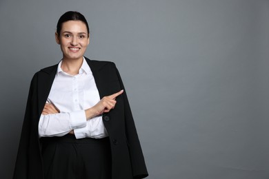 Photo of Confident business woman in suit pointing at something on grey background. Space for text