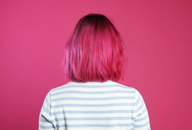 Photo of Woman with beautiful bright dyed hair on pink background, back view