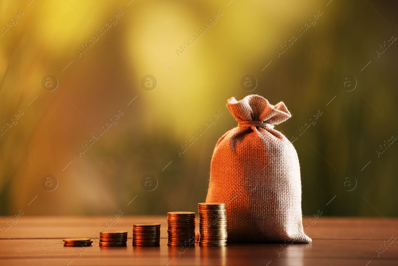Burlap bag and stacked coins on wooden table against blurred background Photo of Burlap bag and stacked coins on wooden table against blurred background
