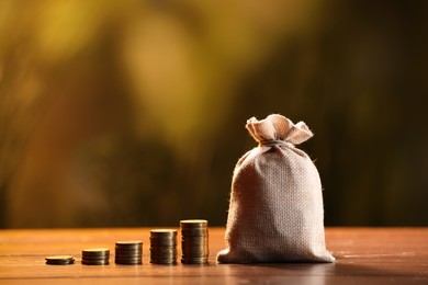 Photo of Burlap bag and stacked coins on wooden table against blurred background