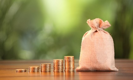 Photo of Burlap bag and stacked coins on wooden table against blurred background