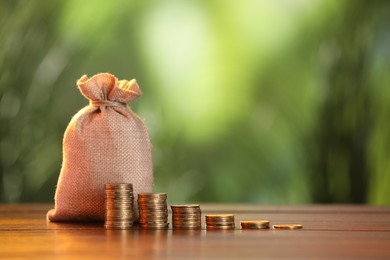 Photo of Burlap bag and stacked coins on wooden table against blurred background