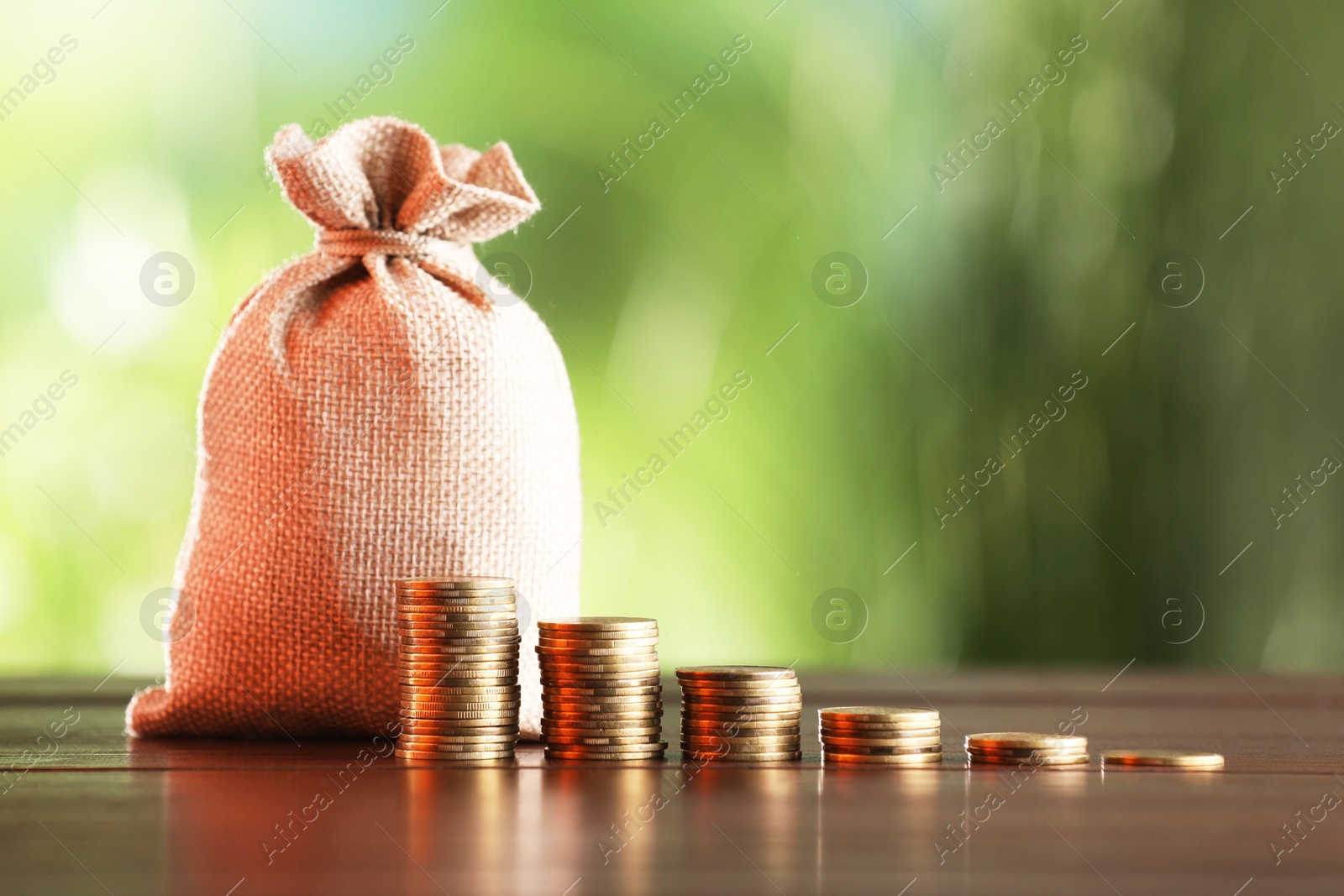 Burlap bag and stacked coins on wooden table against blurred background Photo of Burlap bag and stacked coins on wooden table against blurred background