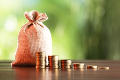 Photo of Burlap bag and stacked coins on wooden table against blurred background