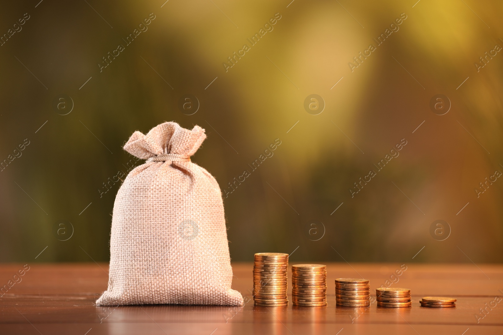 Burlap bag and stacked coins on wooden table against blurred background Photo of Burlap bag and stacked coins on wooden table against blurred background