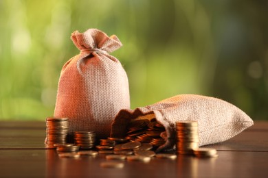 Photo of Burlap bags and stacked coins on wooden table against blurred background