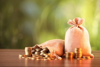 Photo of Burlap bags and stacked coins on wooden table against blurred background