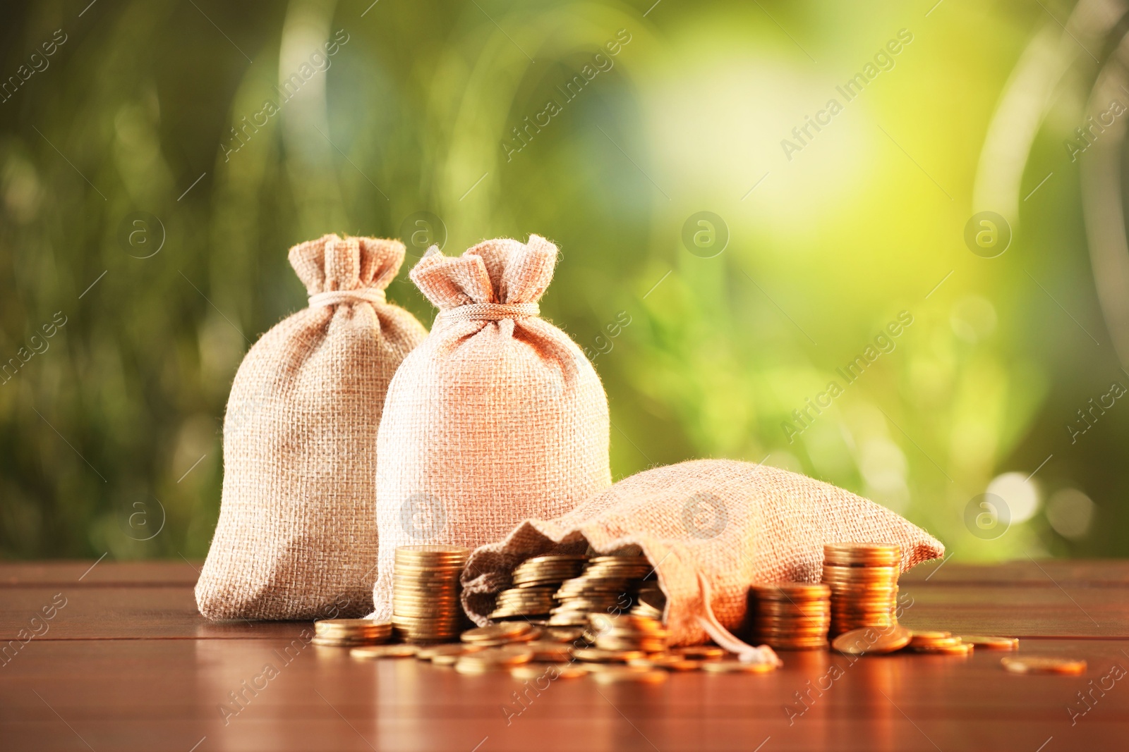 Burlap bags and stacked coins on wooden table against blurred background Photo of Burlap bags and stacked coins on wooden table against blurred background